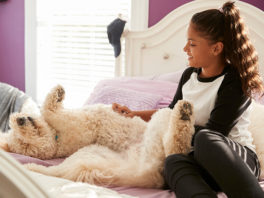 A young teen girl petting her dog on her bed
